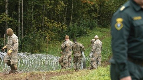 Latvian army servicemen build a temporary fence from a barbed wire on the Latvian-Belarus border ...