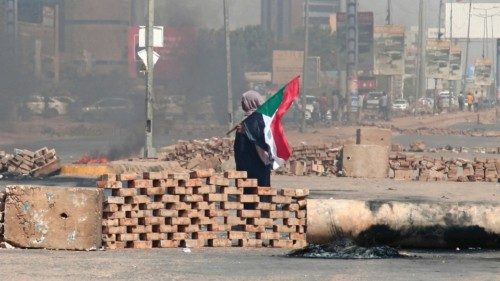 TOPSHOT - A Sudanese demonstrator carrying a national flag walks by roadblocks set up by protesters ...
