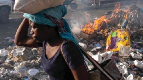 A woman carrying a bag of rice on her head walks past a pile of burning trash during the third day ...