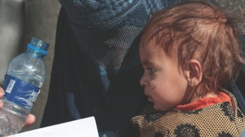 A displaced Afghan woman holds her child as she waits with other women to receive aid supply outside ...