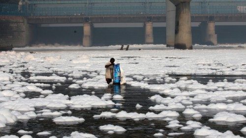 epa09572209 A man throws waste in the polluted Yamuna river that is covered with toxic foam caused ...