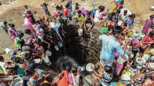 Indian villagers throw containers attached to ropes into a well to collect their daily supply of ...