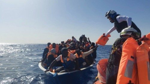 FILE PHOTO: A crew member helps migrants on a wooden boat wait to be rescued by search and rescue ...