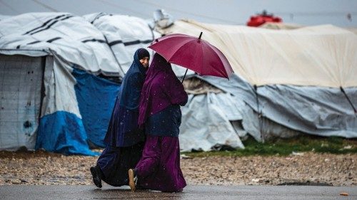 Women use an umbrella as they walk in the rain at Camp Roj, where relatives of people suspected of ...