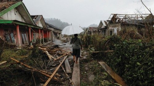 A man with an umbrella walks amongst damaged houses looking for his goat in an area affected by the ...