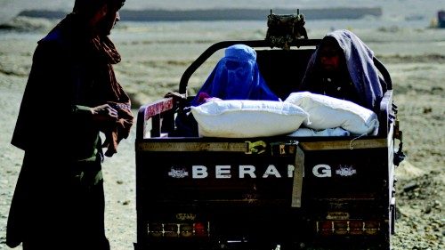 Women sit on the back of a vehicle after collecting food aid distributed by the Red Cross in ...