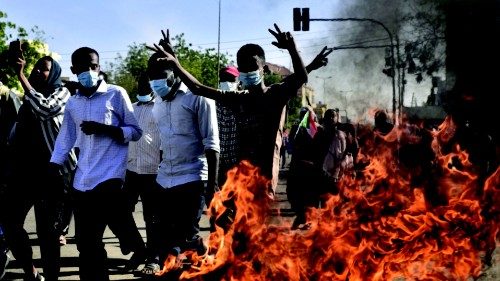 Sudanese protesters flash the victory sign as they walk past burning tyres during a demonstration ...