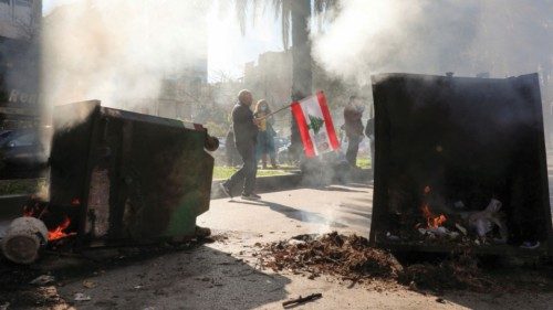 A man holds the Lebanese flag near burning garbage bins during a protest by the family members of ...