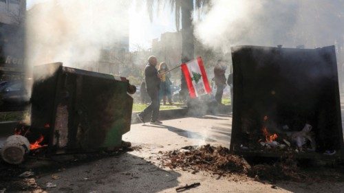A man holds the Lebanese flag near burning garbage bins during a protest by the family members of ... A man holds the Lebanese flag near burning garbage bins during a protest by the family members of ...