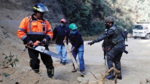 A fireman and some other people remove debris and tree branches next to a landslide and a fallen ...
