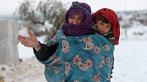 A woman carries a child as they walk in the snow at a camp for internally displaced people in the ...