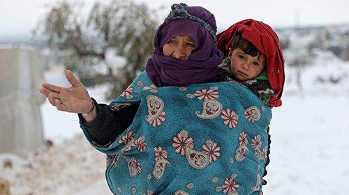 A woman carries a child as they walk in the snow at a camp for internally displaced people in the ... A woman carries a child as they walk in the snow at a camp for internally displaced people in the ...
