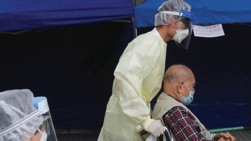 Medical workers wearing personal protective equipment (PPE), transfer a patient on a wheelchair into ... Medical workers wearing personal protective equipment (PPE), transfer a patient on a wheelchair into ...