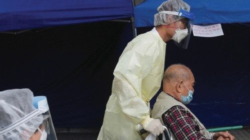 Medical workers wearing personal protective equipment (PPE), transfer a patient on a wheelchair into ...