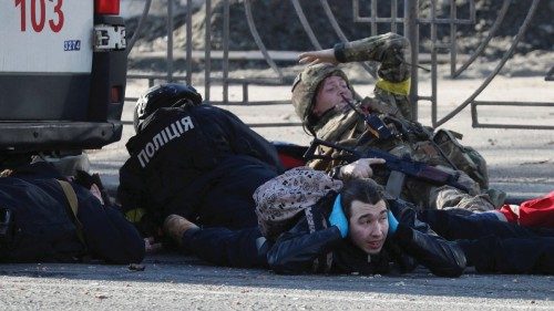 People take cover as an air-raid siren sounds, near an apartment building damaged by recent shelling ...