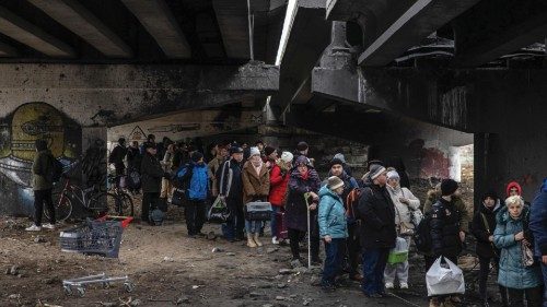 epa09807216 People with their luggage wait under a destroyed bridge as they flee from the frontline ...
