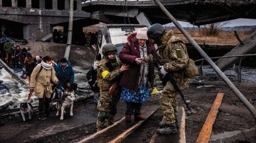 TOPSHOT - Ukrainian soldiers help an elderly woman to cross a destroyed bridge as she evacuates the ...