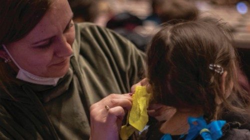 epa09808075 A woman ties ribbons in Ukrainian national flag colors in a girl's hair as people wait ...