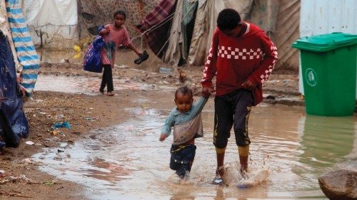 Children walk in flood water outside tents damaged by torrential rain, at a camp for internally ...