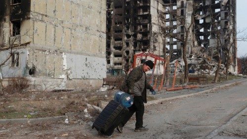 A local resident walks with a suitcase past apartment buildings destroyed during Ukraine-Russia ...