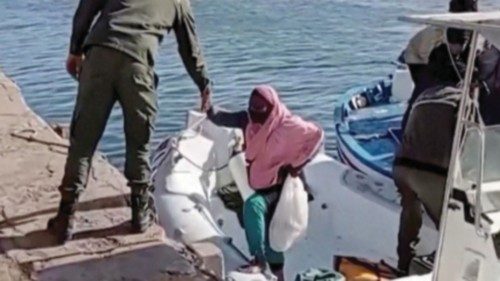 A Tunisian national coast guard helps migrants to get off a rescue boat in Jbeniana, Safx, Tunisia ...