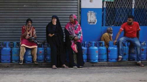 People sit on their empty cylinders as they wait in a queue to buy domestic gas at a distribution ...