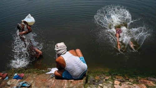 A man washes his clothes as others bathe in a canal on a hot summer afternoon in New Delhi on June ...