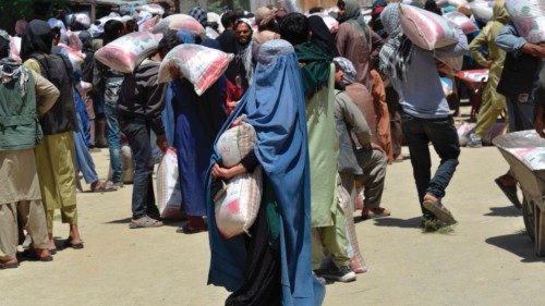 People collect sacks of rice distributed to people in need by the Afghan Ministry of Refugees in ...