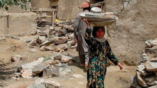 A child carrying utensils on her heads walks past damaged houses are pictured following an ...