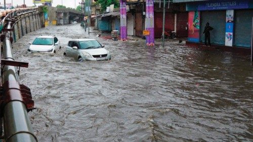 A man (L) watches vehicles stucked in a waterlogged street after heavy rains in Ajmer on July 24, ...