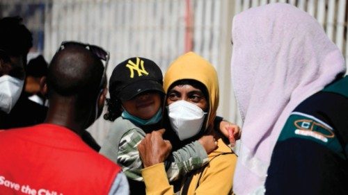 A member of the NGO 'Save the Children' (L) speaks with migrants queuing before boarding a ferry ...