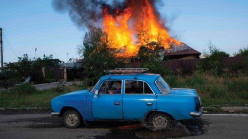 TOPSHOT - A Ukrainien man drives past a burning house hit by a shell in the outskirts of Bakhmut, ...