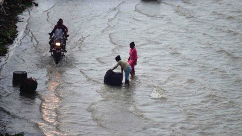 People wade along a flooded street on the banks of river Ganges in Allahabad on August 21, 2022. ...