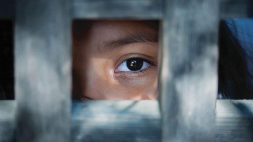 The blank stare of a child's eye who is standing behind what appears to be a wooden frame The blank stare of a child's eye who is standing behind what appears to be a wooden frame
