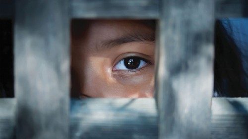 The blank stare of a child's eye who is standing behind what appears to be a wooden frame