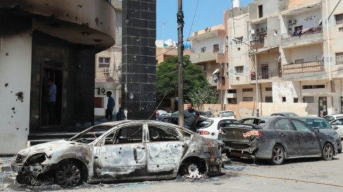 People inspect car carcasses in front of a damaged building following clashes between backers of ...