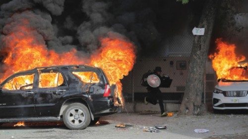 A man runs with looted goods near cars on fire during protests over rising fuel prices and crime as ...