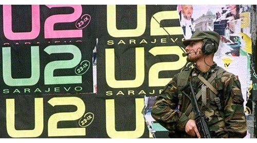 An Italian peacekeeper holds his rifle as he stands in front of wall covered with U2 posters in ...