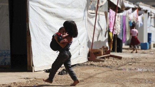 A Syrian refugee girl carries a child as she walks past tents at an informal camp, in the Bekaa ...