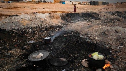 Cooking pots are placed on fire amidst the remains of asphalt at the Sahlah al-Banat camp for ...