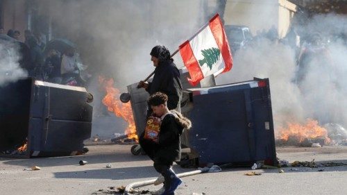 A protestor holding the Lebanese flag walks near burning barricades during a protest over economic ...