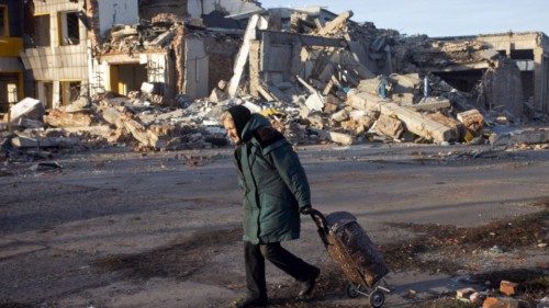 An elderly woman pulls a trolley bag past a destroyed building in Bakhmut, Donetsk region, on ...