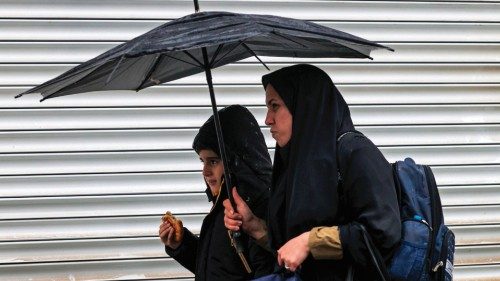 A woman and a boy walk with an umbrella past a closed shop at Enghelab Square in Iran's capital ...
