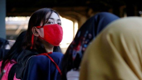 A woman wearing protective mask looks on as she waits for a commuter train at a station in Jakarta, ...