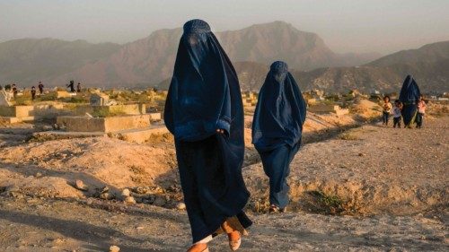 In this picture taken on July 19, 2022, Afghan women wearing traditional burqas walk past a cemetery ...
