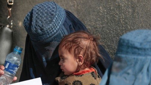 FILE PHOTO: A displaced Afghan woman holds her child as she waits with other women to receive aid ...