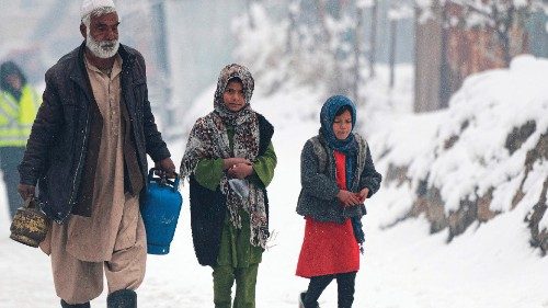 A man carrying gas canisters walks next to children along a street during snow fall in Kabul on ...