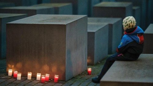 epa10431497 Mourning candles are placed around steles as a young boy sits next to the scene during a ...