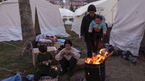 A Syrian family gathers around a fire for warmth, at a park turned into a camp for displaced people, ...