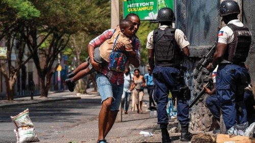 A person carries a child past Haitian National Police attempting to repel gangs in a neighborhood ...